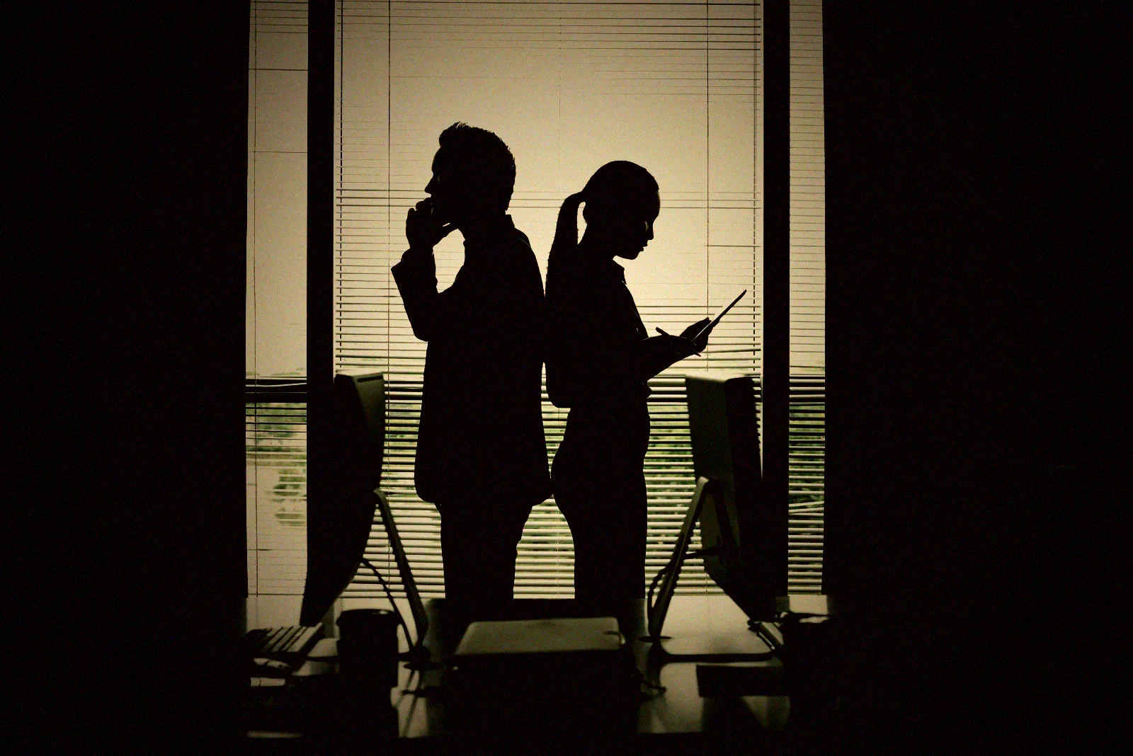 Two silhouetted figures at a lit office threshold, the moment where every physical access decision is actually made.