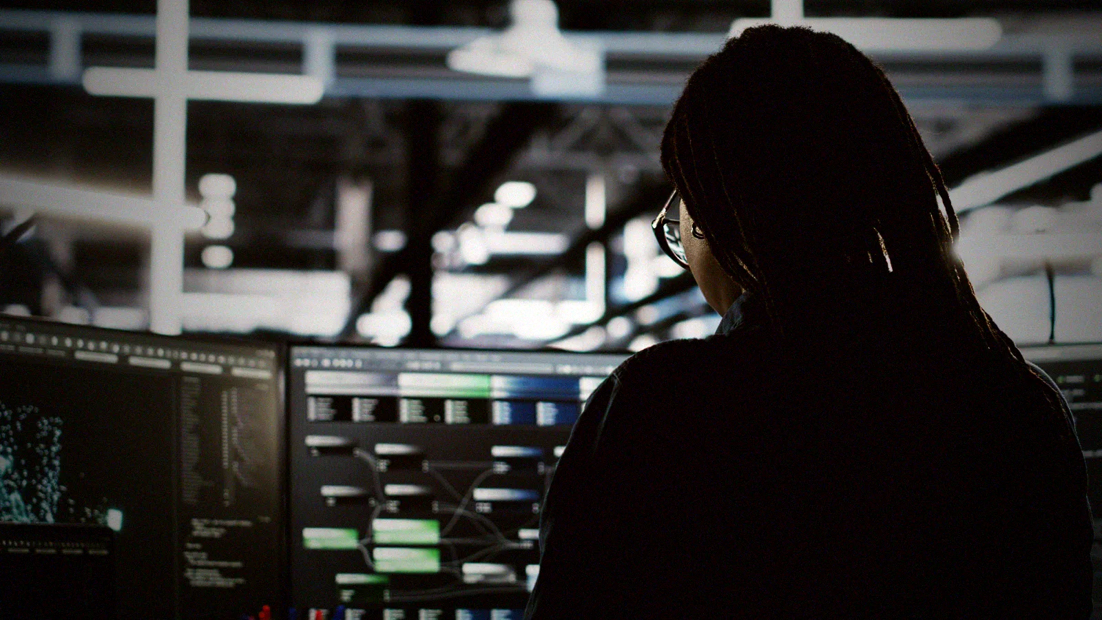 An operator at a dark terminal, an AI coding tool session open across two screens.